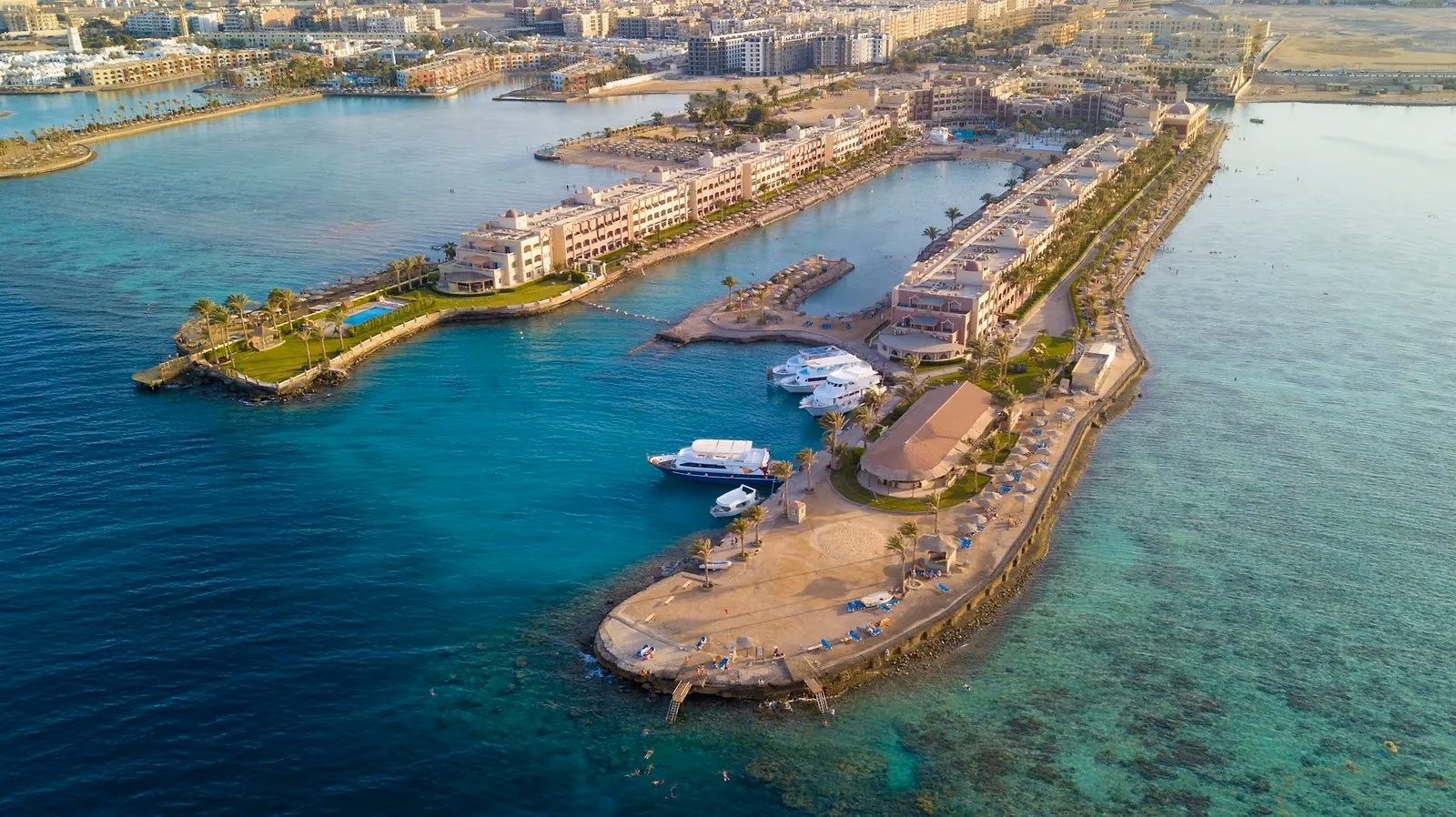 Luchtfoto van een jachthaven met hotelgebouwen op smalle landtongen in turquoise water