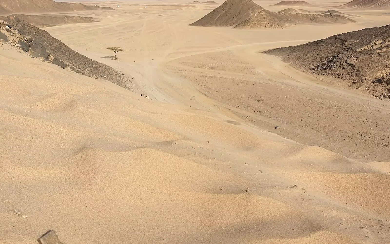 Een woestijnlandschap met zandduinen en rotsachtige heuvels onder een heldere lucht