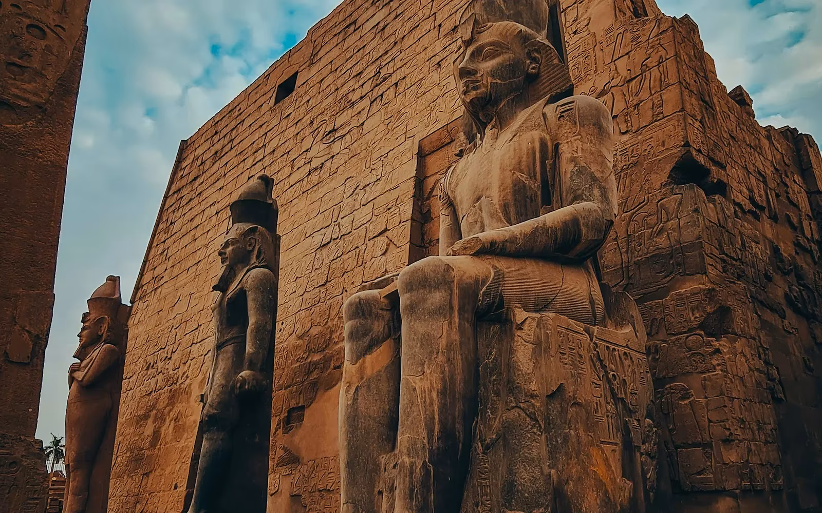 Kolossale zittende beelden voor de ingang van een oude tempel in Luxor onder een bewolkte lucht
