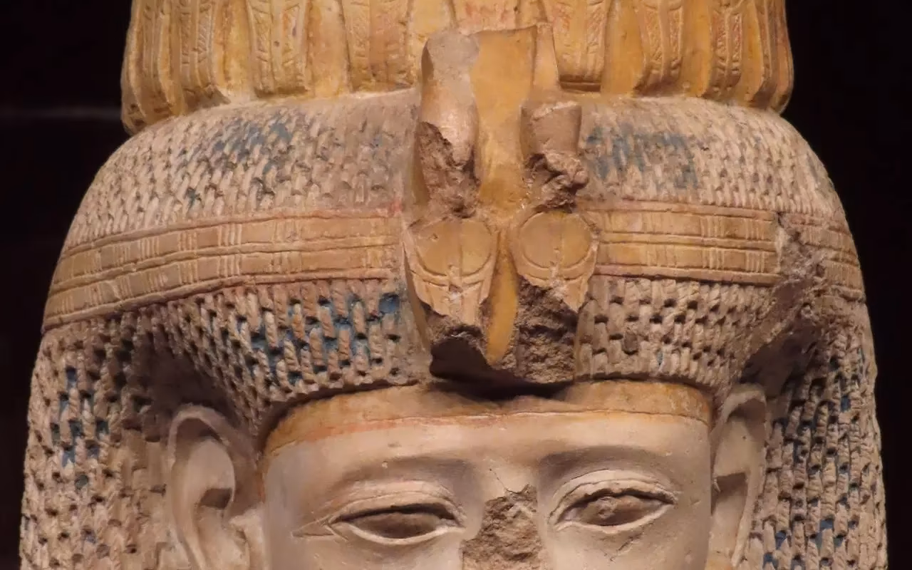 Het gezicht van een Egyptisch beeld met een gevlochten kapsel en een kroon van gestileerde figuren
