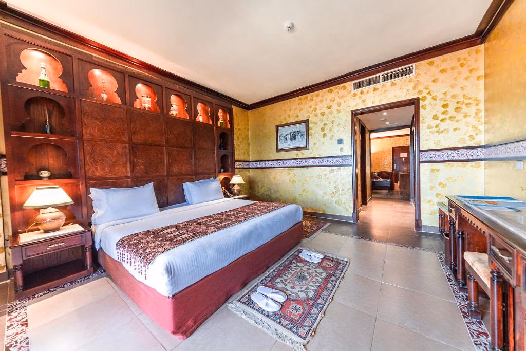 Slaapkamer met een kingsize bed, houten wandkasten met verlichte nissen en een doorgang naar de woonkamer bij Sentido Mamlouk Palace Resort in Hurghada