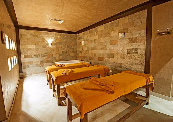 Behandelkamer met drie massagetafels met oranje doeken en natuurstenen wanden in de spa van Sentido Mamlouk Palace in Hurghada