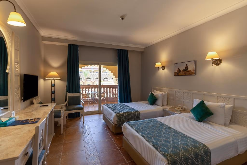 Kamer met twee losse bedden, een bureau met televisie en een balkon met zicht op een woonblok bij Sentido Mamlouk Palace in Hurghada