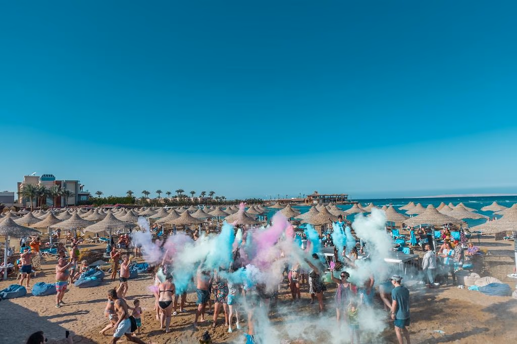 Gasten op het strand tijdens een kleurpoederfeest onder rieten parasols bij Sentido Mamlouk Palace in Hurghada