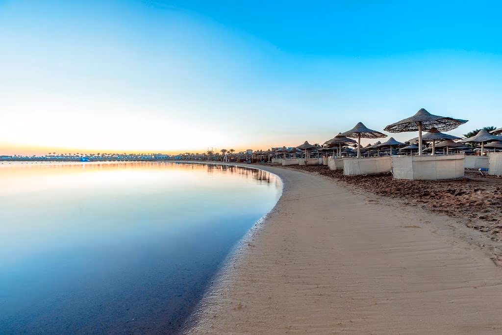 Rustig zandstrand met rieten parasols en witte windschermen bij zonsopkomst bij Sentido Mamlouk Palace in Hurghada