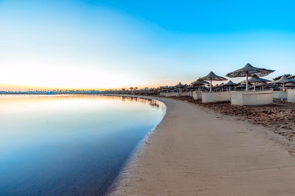 Rustig zandstrand met rieten parasols en witte windschermen aan een kalme baai bij zonsopkomst bij Sentido Mamlouk Palace in Hurghada