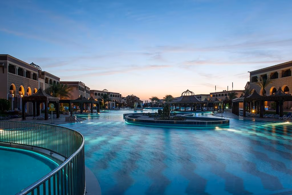 Verlicht lagunezwembad met een eiland en houten paviljoens in de schemering bij Sentido Mamlouk Palace in Hurghada