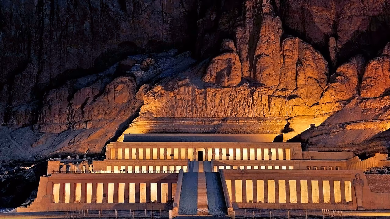 De verlichte terrassentempel van Hatshepsut tegen een rotswand bij Luxor in de avond